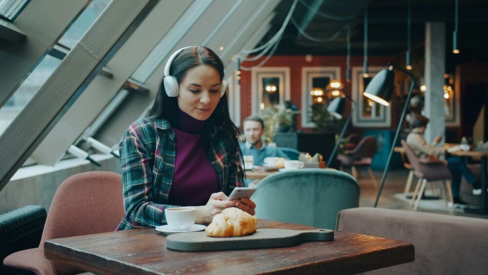 ヘッドホンをつけてカフェでスマホのAI英語学習アプリを使う女性